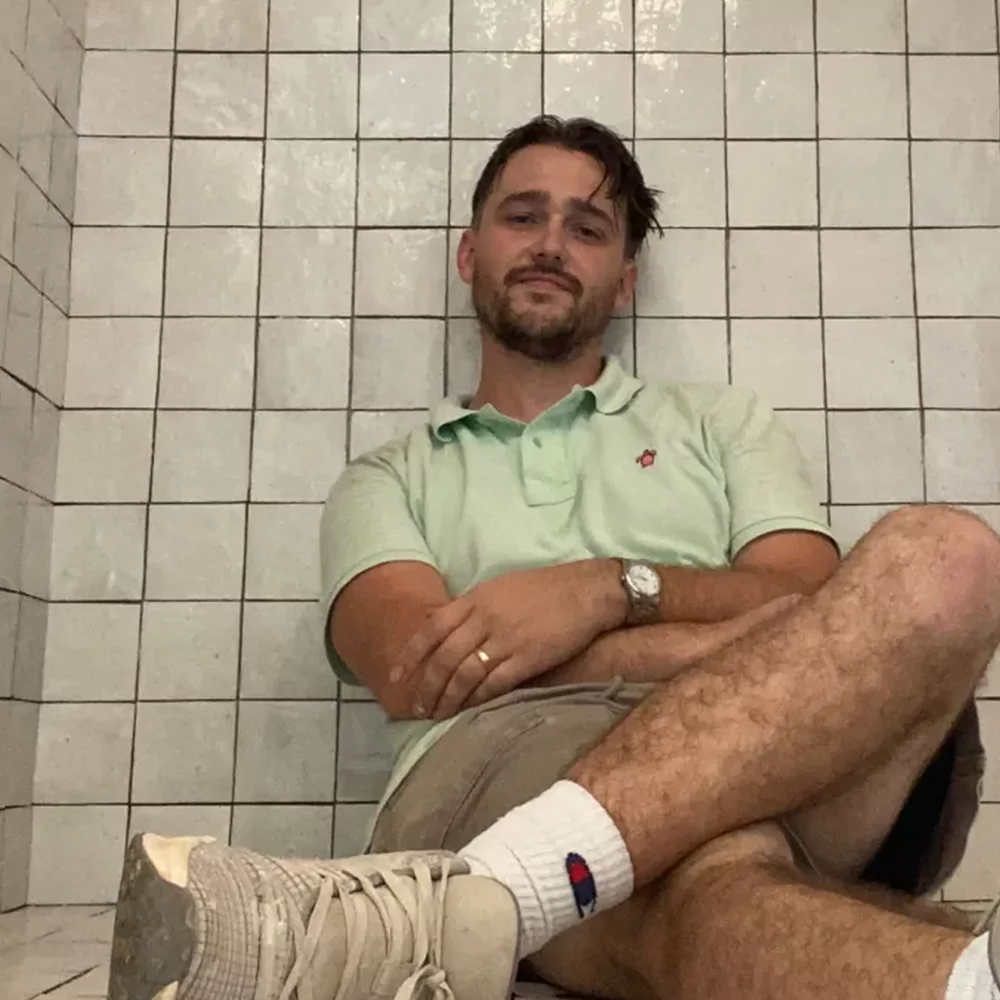 Brad Fleitz, owner of Aesthetic Tile, sitting in a finished white zellige tile shower