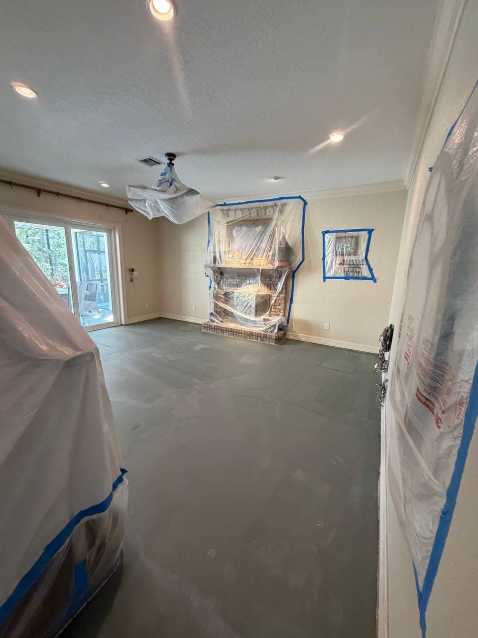Prepared floor in a room with a fireplace and surfaces covered in taped plastic