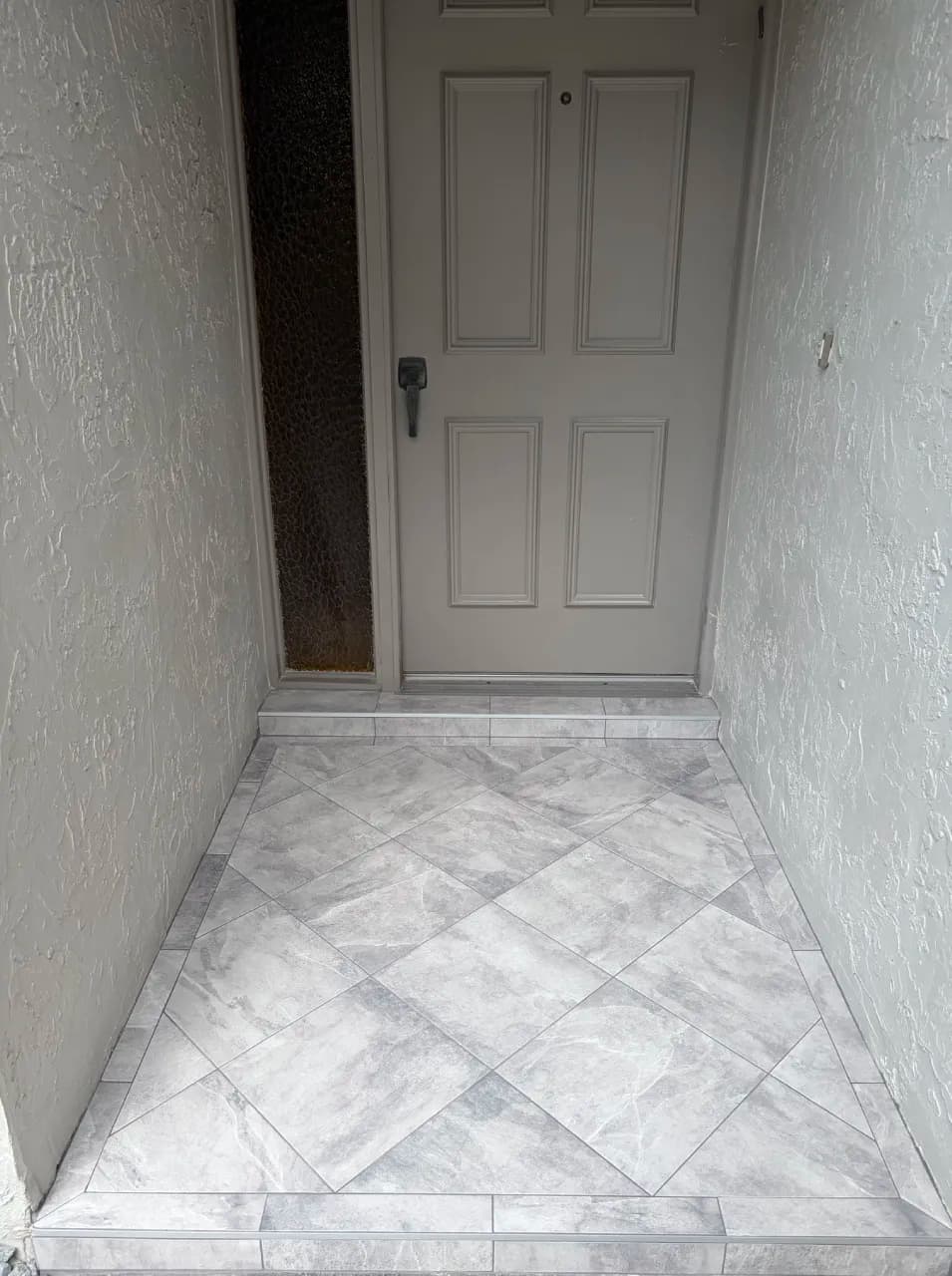 Gray porcelain entry tiles laid diagonally inside a straight border