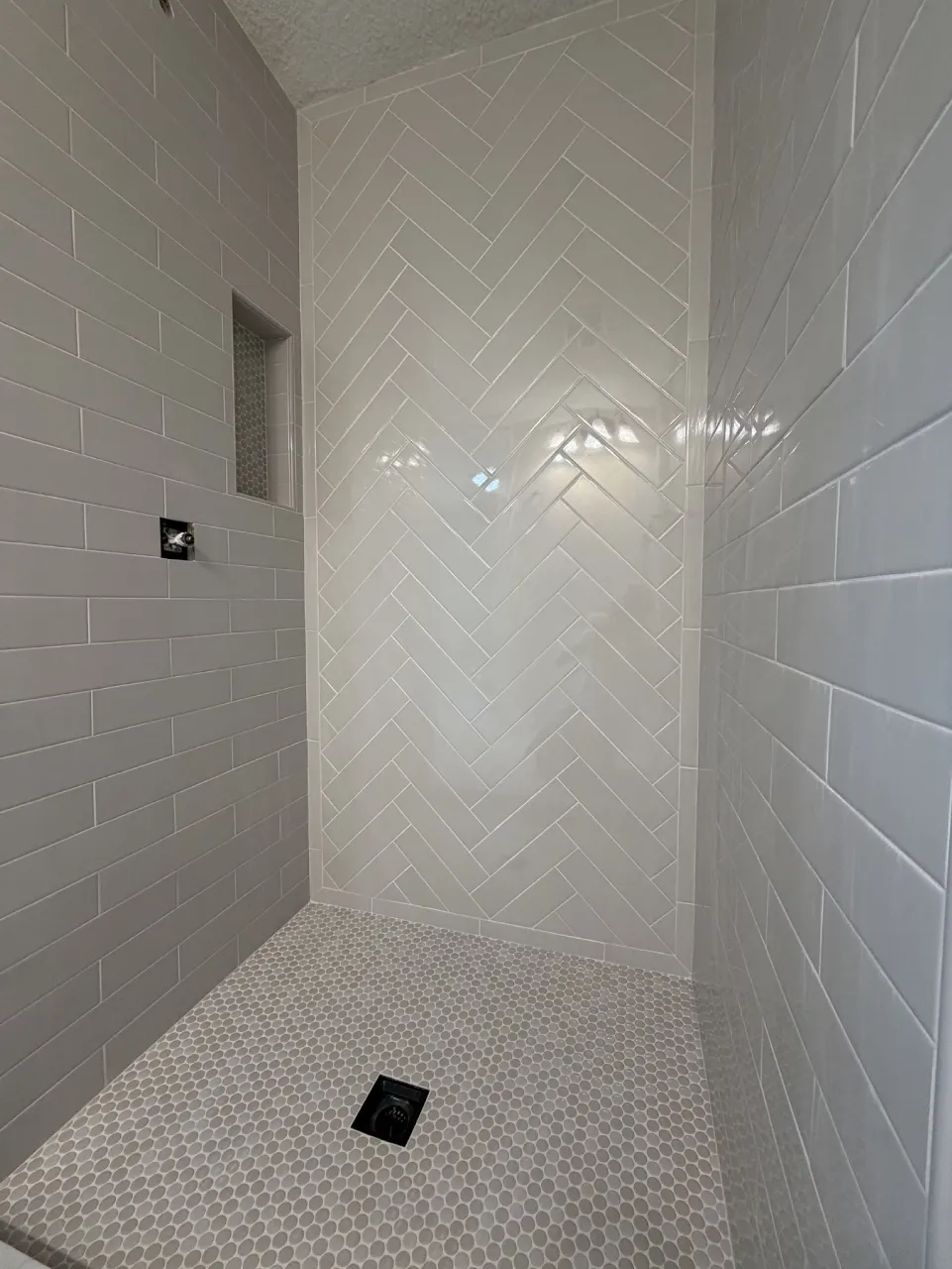 Completed ceramic shower with a herringbone accent wall and mosaic floor