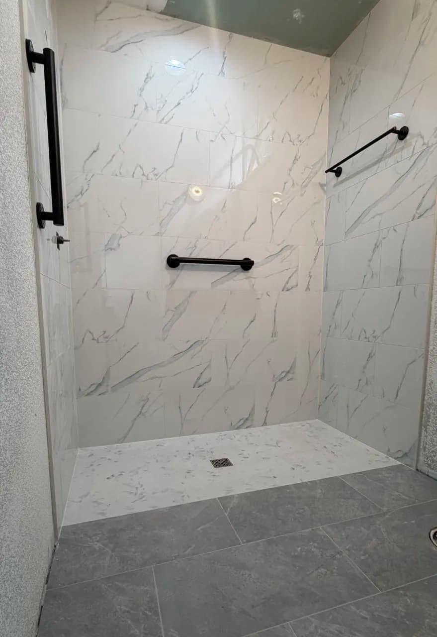 Completed curbless shower with light wall tile and dark grab bars
