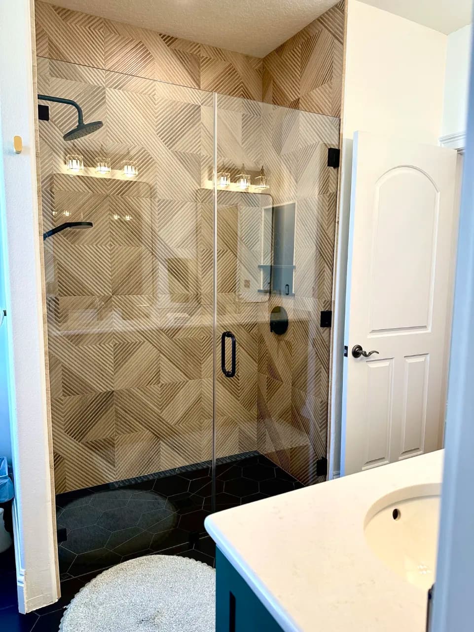 Glass shower enclosure with patterned walls and a dark hex tile floor