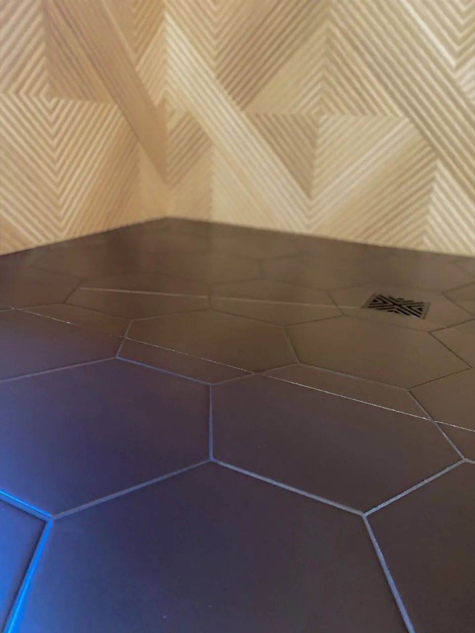 Dark hexagonal shower floor with a decorative drain grate