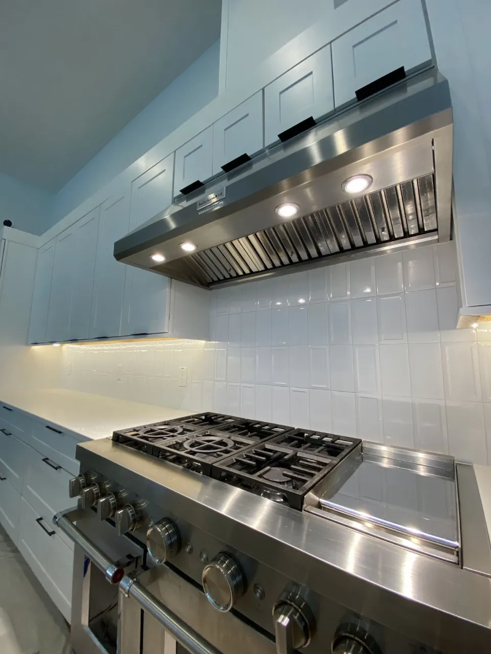Close view of the varied white ceramic backsplash beneath cabinet lighting