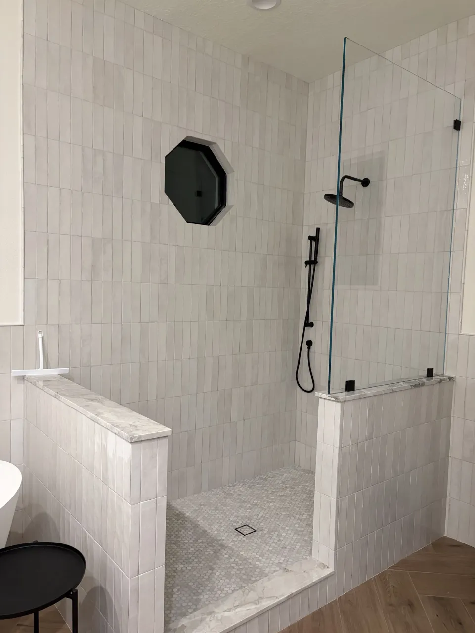 Completed light-tile shower with glass enclosure and an octagonal window