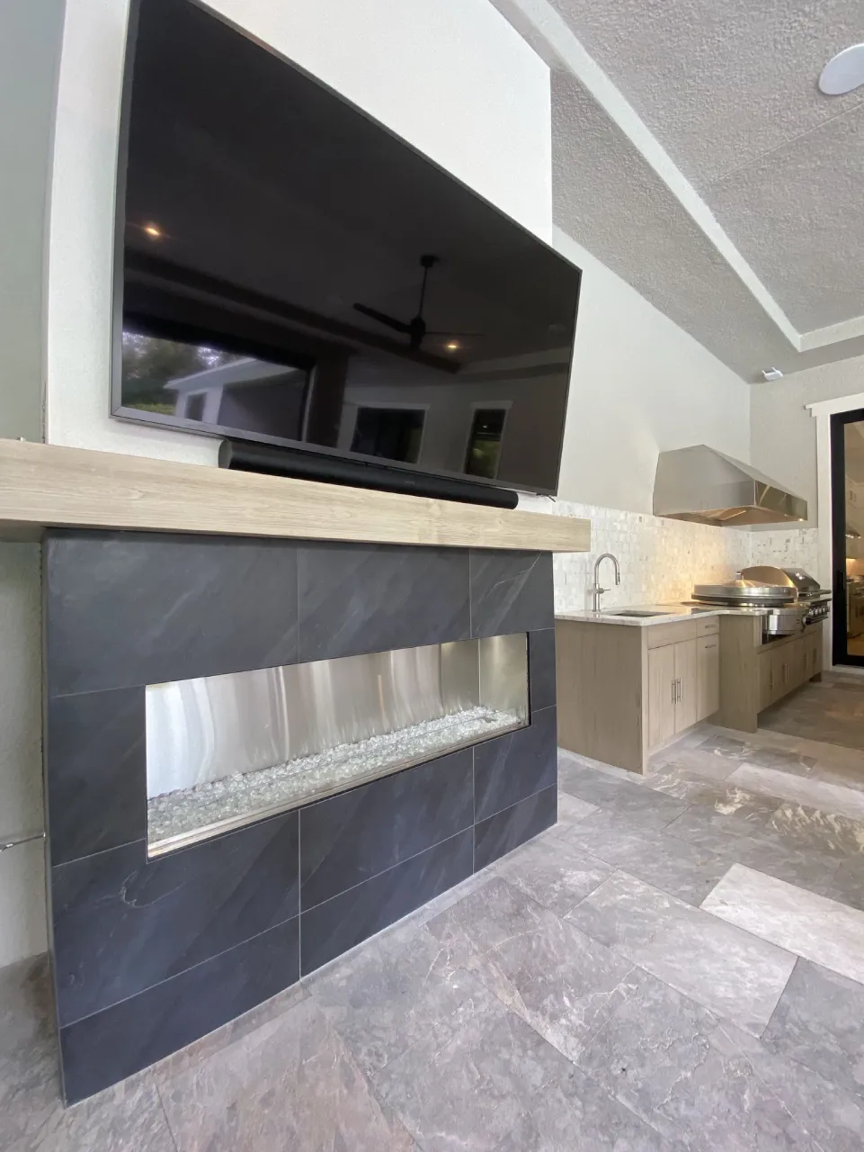 Dark porcelain outdoor fireplace beneath a television beside the outdoor kitchen