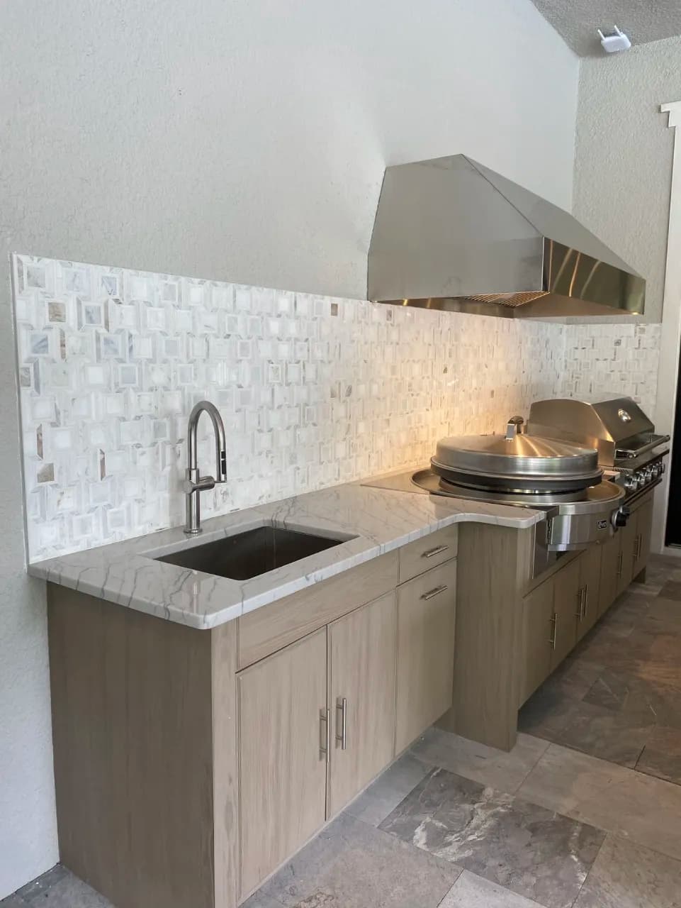 Light marble mosaic backsplash behind the outdoor sink and cooking area