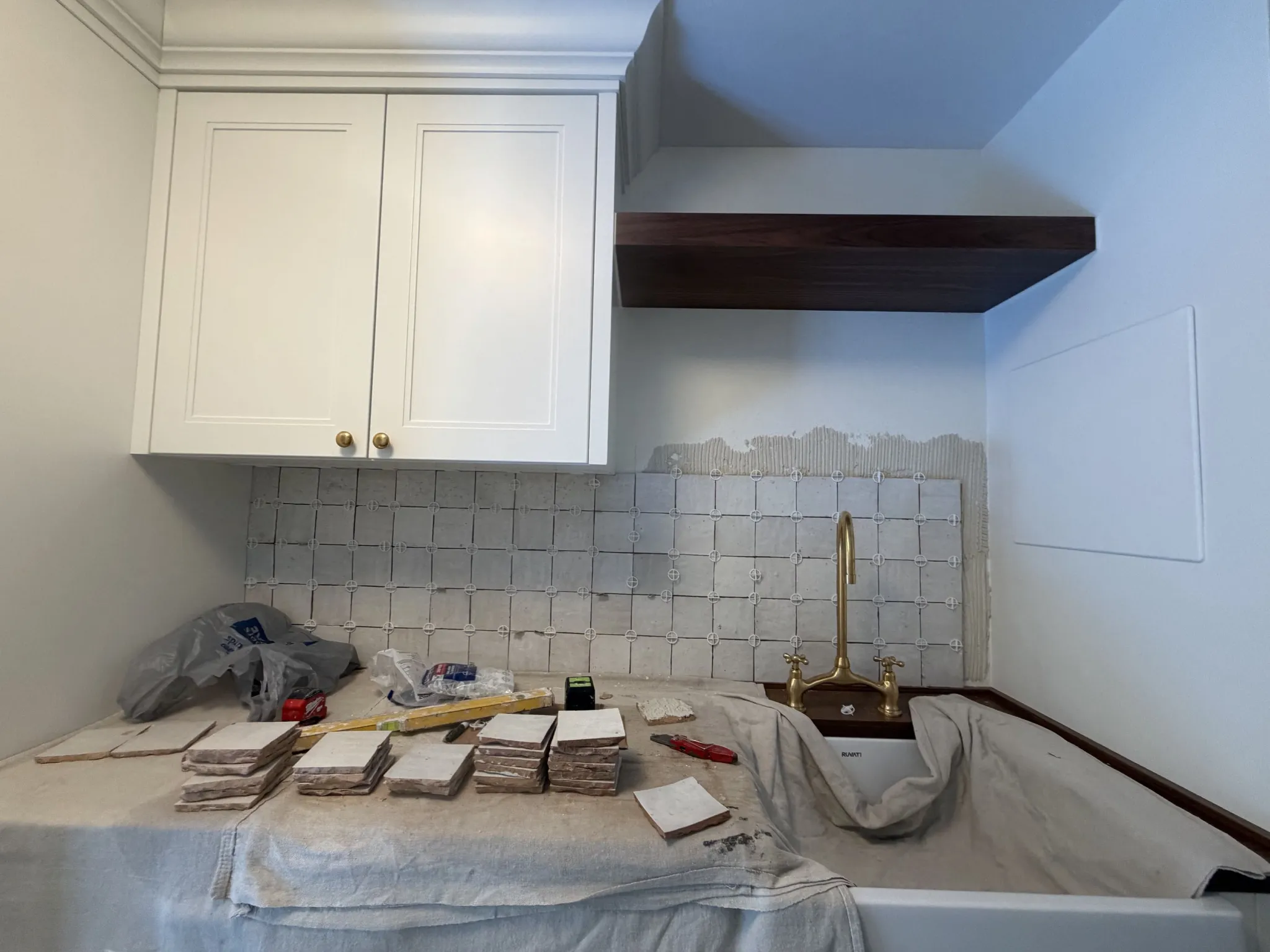 Backsplash installation in progress with tiles and tools on a protected counter