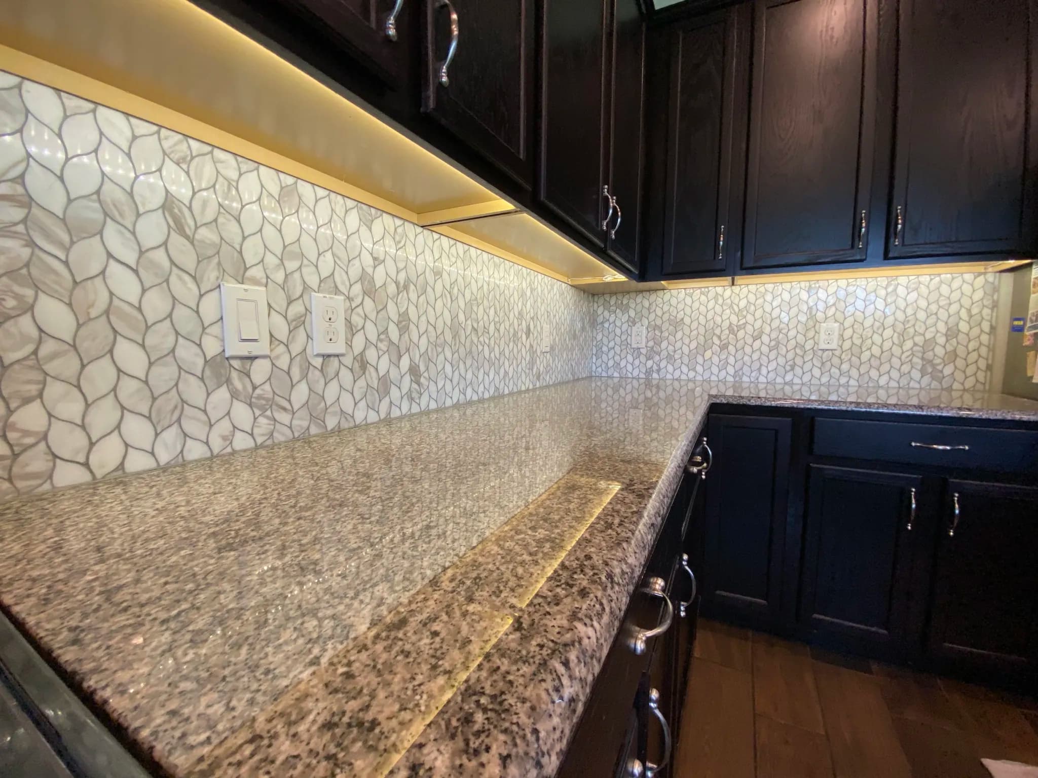 Marble leaf mosaic along the counter beneath dark kitchen cabinets