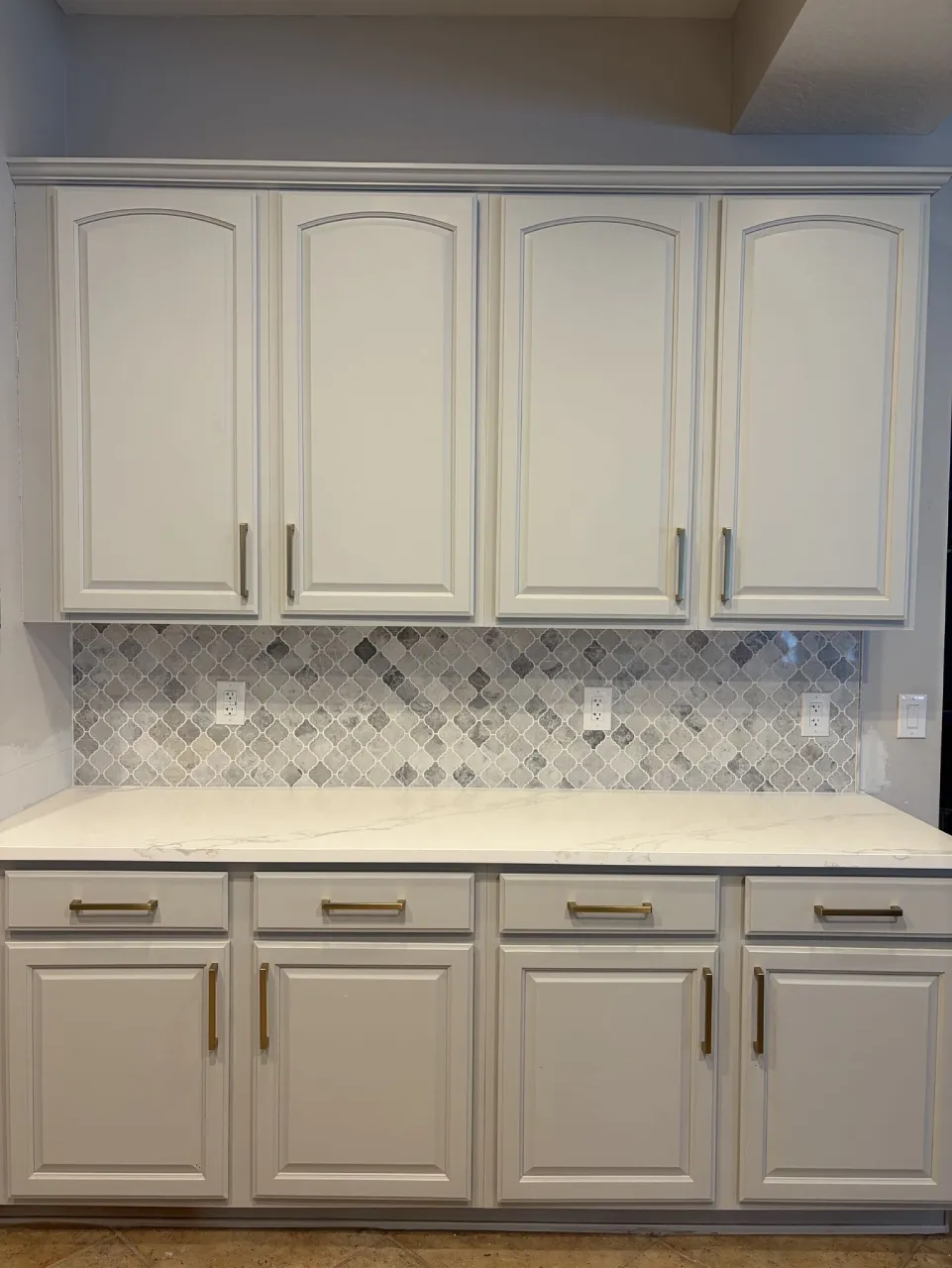 Marble mosaic backsplash beneath light cabinets with white grout